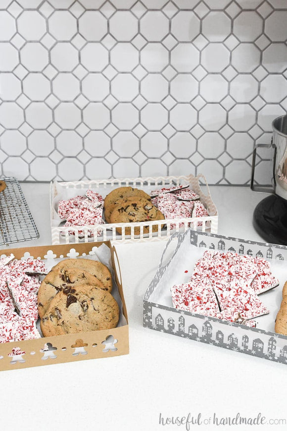 Three different designs on the sides of the paper trays filled with cookies and peppermint bark.