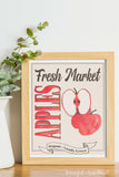 Fresh market apples farmers market sign in a frame next to a white vase.
