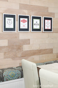 Four printable Christmas signs on the wall in a dining room.